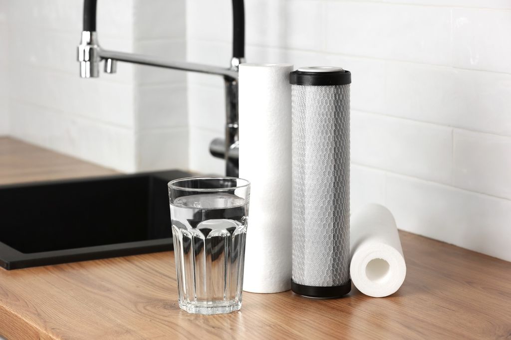 Glas Leitungswasser neben Filterkartuschen für einen Untertisch-Wasserfilter in der Küche